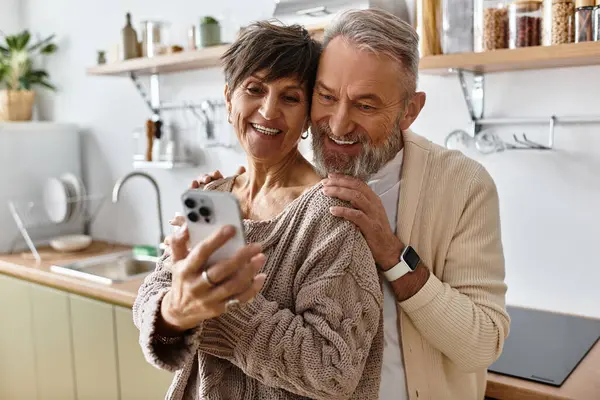 Um casal feliz compartilha um momento terno, olhando para o telefone em um ambiente de cozinha quente. — Fotografia de Stock