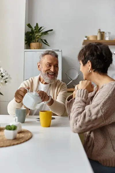 A mature couple shares laughter and conversation while sipping coffee at their kitchen table. — Stock Photo