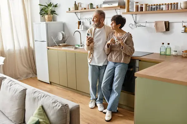 Una pareja madura disfruta de la compañía de los demás mientras bebe en un ambiente cálido de la cocina. - foto de stock