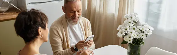 Mature couple shares smiles and laughter while looking at a device in their cozy home. — Stock Photo