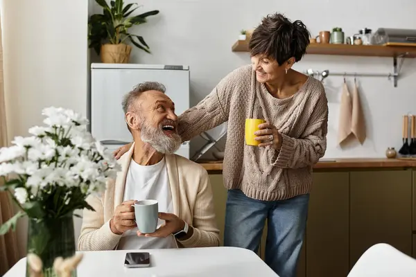 A mature couple shares laughter and warmth over cups of coffee in their inviting kitchen. — Stock Photo