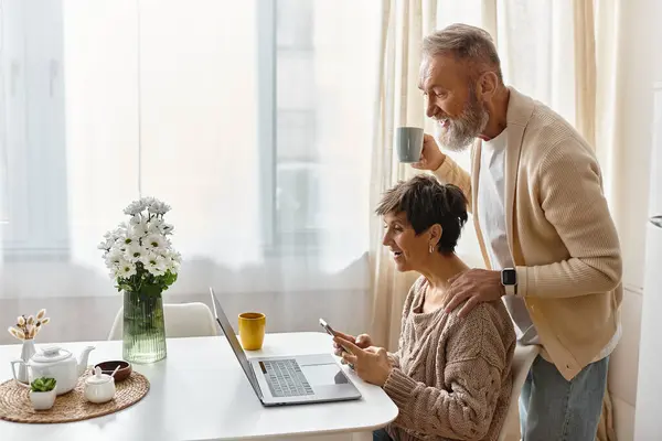 Uma mulher e um homem desfrutam de seu tempo junto com café, um laptop e um telefone em uma sala brilhante. — Fotografia de Stock