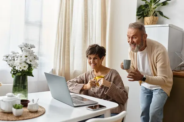 Ältere Paare genießen einander Gesellschaft beim Surfen auf ihrem Laptop in einer sonnigen Küche. — Stockfoto