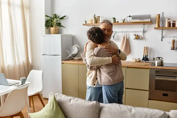 A mature couple shares a warm hug in their bright kitchen filled with plants and kitchenware. — Stock Photo