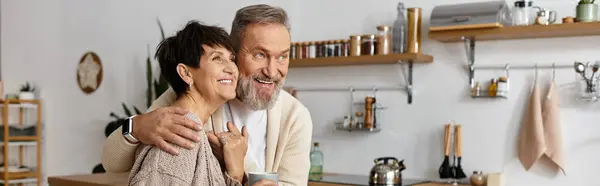 Un couple heureux partage une étreinte joyeuse dans leur charmante cuisine remplie de lumière chaude. — Photo de stock