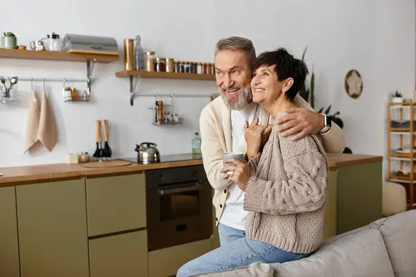 A mature couple smiles lovingly while enjoying a warm drink in their cozy kitchen. — Stock Photo