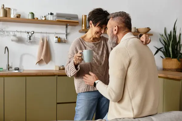 A mature couple shares a joyful moment while enjoying coffee in their warm kitchen. — Stock Photo