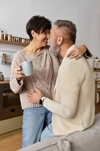 A joyful mature couple enjoys a tender embrace while sharing laughter and drinks at home — Stock Photo