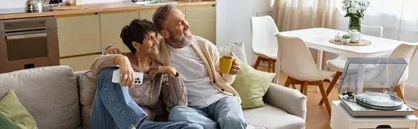 Homem e mulher idosos compartilham um momento delicioso no sofá, bebendo bebidas e relaxando juntos. — Fotografia de Stock