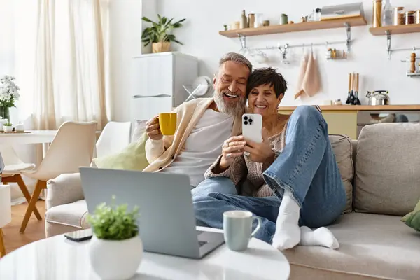 A happy couple relaxes on a couch, savoring drinks and sharing a joyful moment while browsing. — Stock Photo