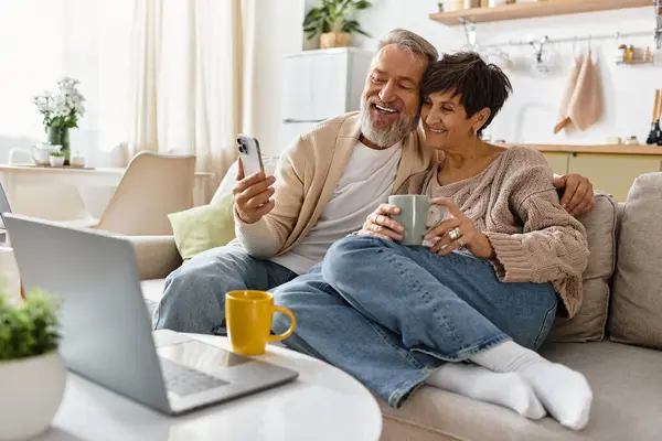 A happy couple relaxes on a sofa, enjoying warm drinks and each others company. — Stock Photo