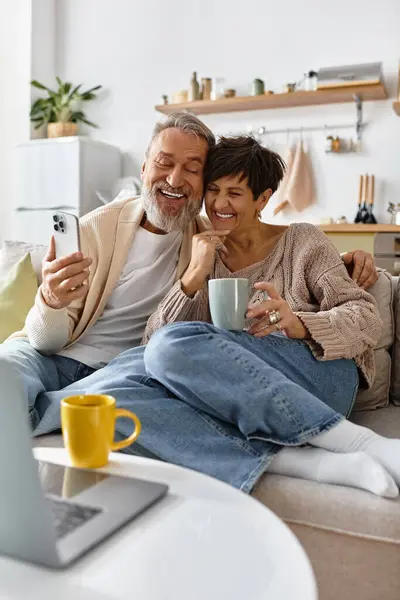 Senior man and woman enjoying a warm drink together while smiling at a smartphone. — Stock Photo