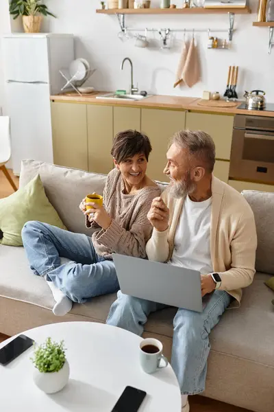 Couple shares smiles and drinks while working together on a laptop in their living room. — Stock Photo