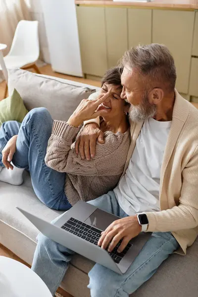 Mature couple shares laughter and affection while using a laptop on their comfortable sofa. — Stock Photo