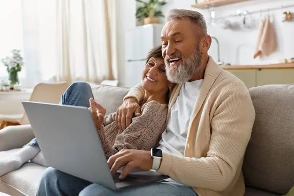 A senior couple share joy as they explore content on a laptop in their cozy living room. — Stock Photo