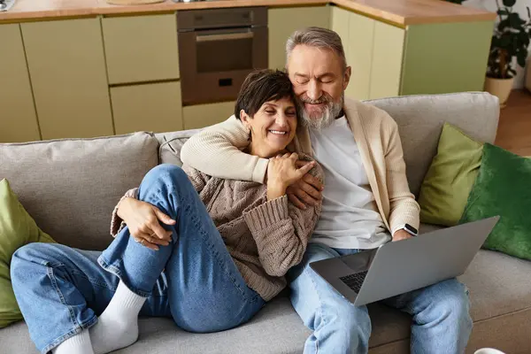 Joyful couple sharing a warm embrace while using a laptop on a comfy sofa in their living room — Stock Photo
