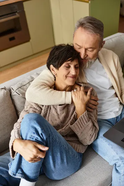 A mature couple relaxes on a sofa, sharing a warm embrace and joyful smiles in their home. — Stock Photo