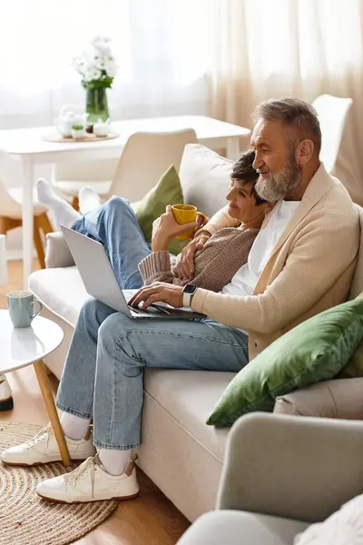 La pareja de ancianos se relaja en un cómodo sofá, compartiendo momentos cálidos y explorando Internet. - foto de stock