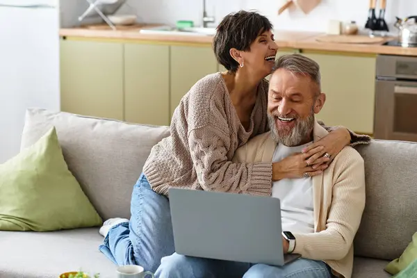 Couple laughs together on a cozy sofa while browsing online in their modern home. — Stock Photo