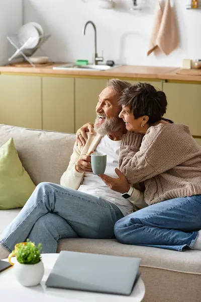 A mature couple enjoys a warm beverage together, smiling in a cozy home setting. — Stock Photo