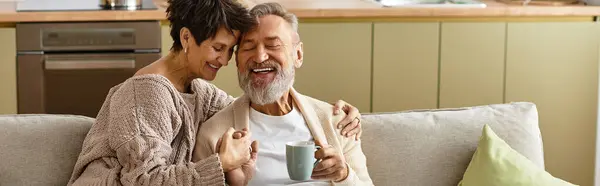 A mature couple relaxes on a couch, sharing laughter and warmth during a peaceful afternoon. — Stock Photo