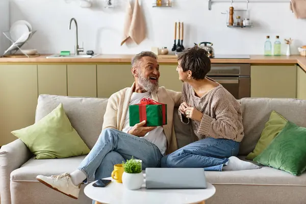 A cheerful couple exchanges gifts in their cozy kitchen, radiating love and happiness together. — Stock Photo