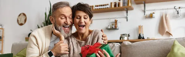 Happy couple sharing a joyful moment as they unwrap a beautifully wrapped gift indoors. — Stock Photo