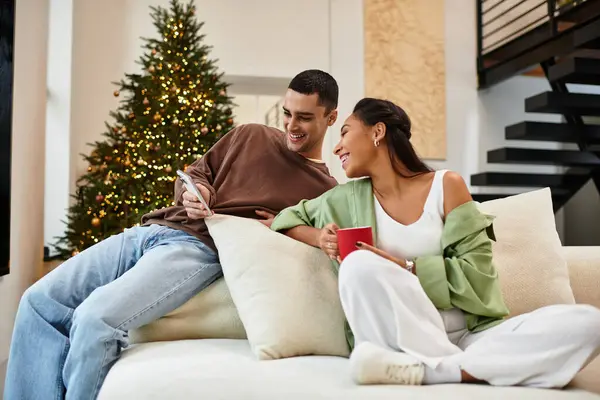A couple relaxes in their cozy apartment, surrounded by Christmas decorations and lights. — Stock Photo