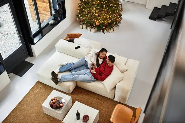 A lovely couple relaxes together with red wine in their stylish living room, enjoying the festive atmosphere. — Stock Photo