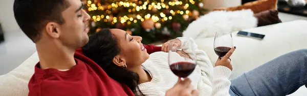 A couple relaxes together, sipping wine in their stylish living room, surrounded by Christmas cheer, banner — Stock Photo