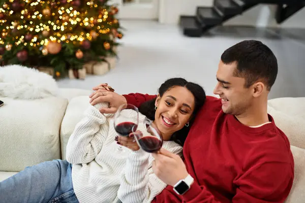 A beautiful couple shares laughter and joy while enjoying wine in their decorated living room. — Stock Photo