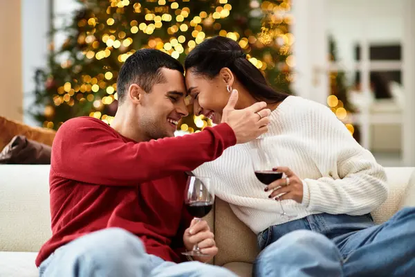 A beautiful couple shares laughter and love over glasses of wine in their festive living room. — Stock Photo