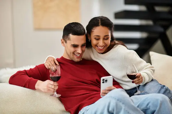 Pareja festiva comparte sonrisas mientras se relaja con el vino en su espacio vital bellamente decorado - foto de stock