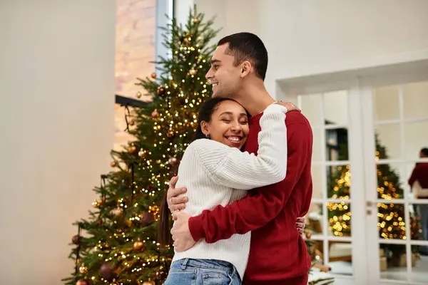 A couple smiles and embraces in their cozy, decorated apartment for the holidays. — Stock Photo