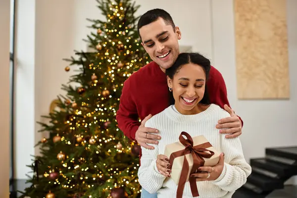 A lovely couple enjoys the holiday spirit in their modern living room, unwrapping gifts together. — Stock Photo