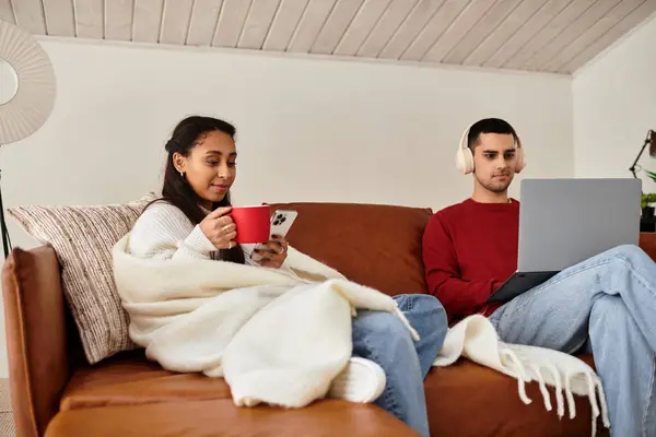 Un couple partage la chaleur sur un canapé, en utilisant des gadgets dans un cadre d'hiver chic. — Photo de stock