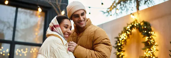 A joyful couple embraces warmly outdoors, surrounded by festive decorations and lights, banner — Stock Photo