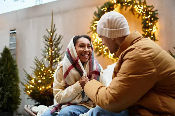 Una bella coppia condivide un momento accogliente all'aperto, vestita calorosamente con luci festive intorno. — Foto stock