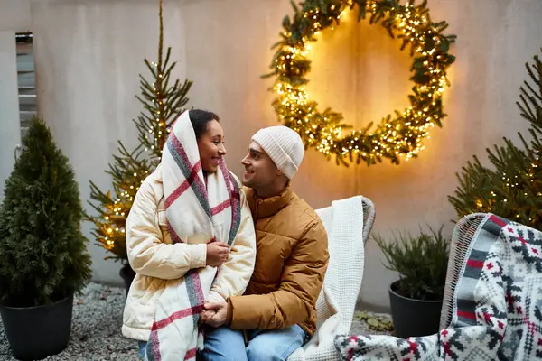 A lovely couple in winter attire enjoys each others company by Christmas lights outdoors. — Stock Photo