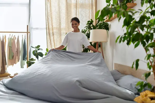 A young African American woman joyfully makes her bed in a stylish and bright apartment. — Stock Photo