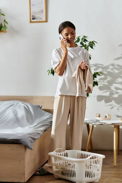 Une jeune afro-américaine range son appartement moderne tout en bavardant au téléphone. — Photo de stock
