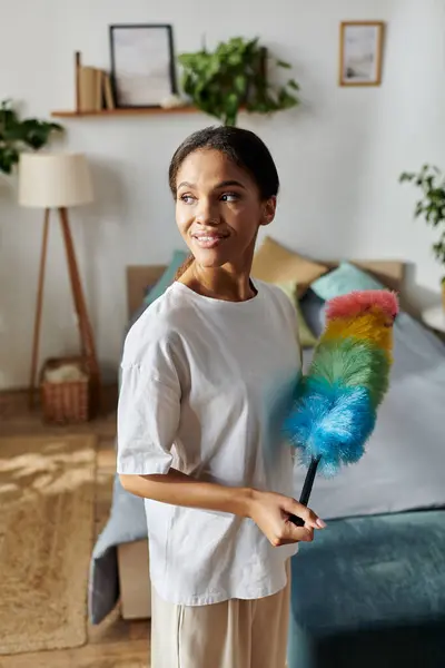 In a bright apartment, a young African American woman joyfully dusts while cleaning her home. - foto de stock