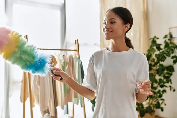 Uma jovem mulher afro-americana sorri enquanto limpa seu elegante apartamento com cuidado. — Fotografia de Stock