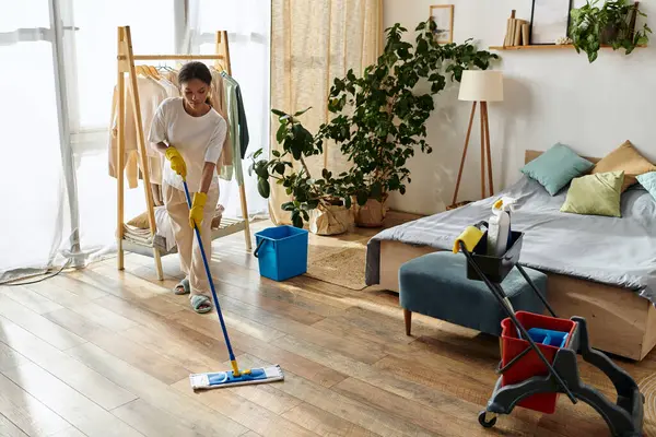 A young African American woman tidies her home while cleaning the wooden floor in her apartment. — Stock Photo