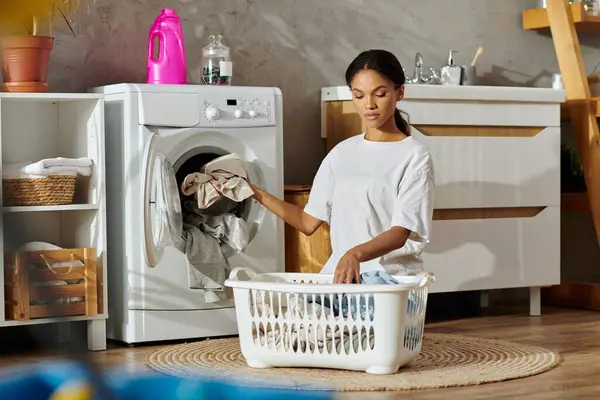 A young African American woman carefully sorts laundry in her stylish apartment space. — Stock Photo
