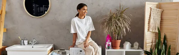 In a modern apartment, a young woman takes a break from her cleaning chores, surrounded by plants, banner — Stock Photo