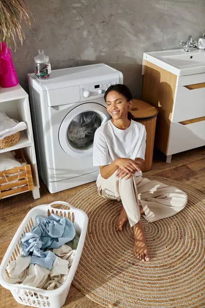 In einer modernen Wohnung entspannt sich eine junge afrikanisch-amerikanische Frau beim Wäschewaschen und lächelt. — Stockfoto