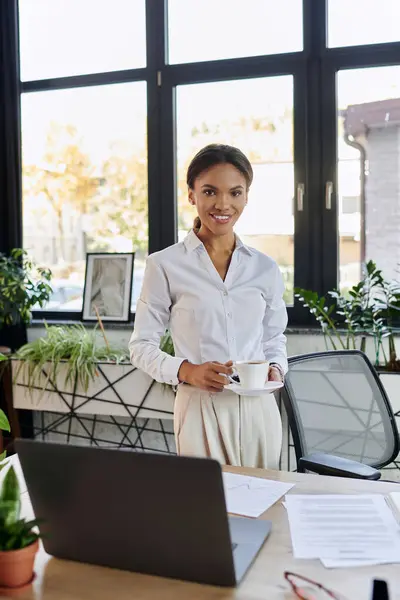 Bright and airy office filled with plants where a young businesswoman stands with coffee. — Stock Photo