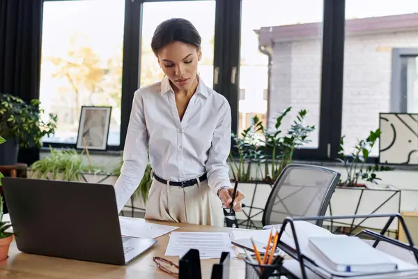 A young professional reviews documents while standing at her desk in a bright office. — Stock Photo