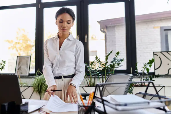 A dedicated young businesswoman reviews documents in her bright office space filled with plants. — Stock Photo